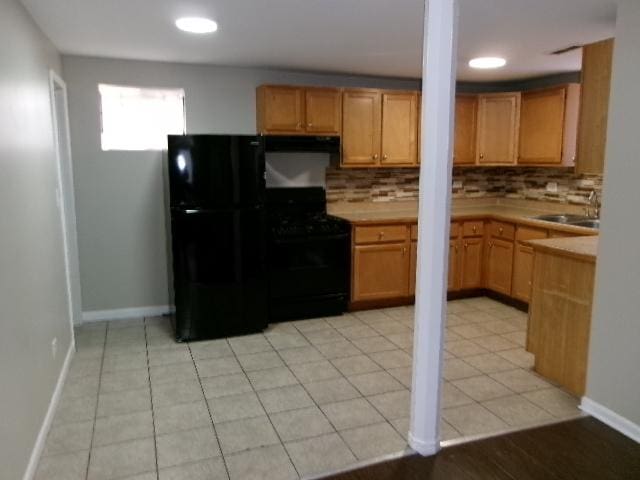 kitchen with black appliances, a sink, tasteful backsplash, light countertops, and under cabinet range hood