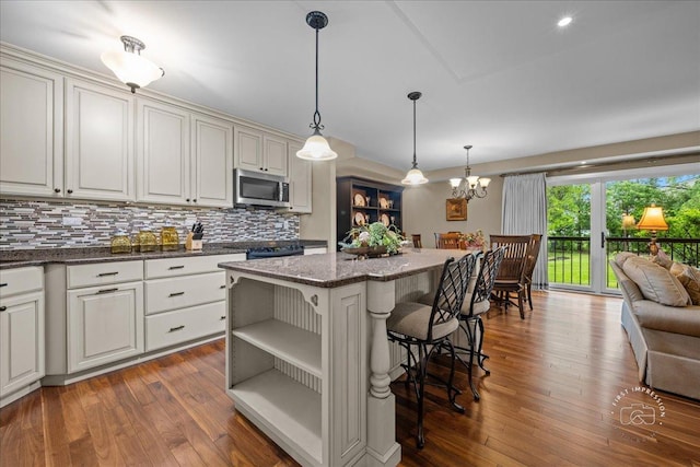1103 N Mill St Unit 111, Naperville, IL 60563 - kitchen featuring stainless steel microwave, open shelves, tasteful backsplash, a kitchen bar, and dark wood finished floors