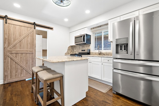 5708 W 82nd Pl, Burbank, IL 60459 - kitchen featuring appliances with stainless steel finishes, a barn door, a kitchen island, a kitchen bar, and dark wood-style floors