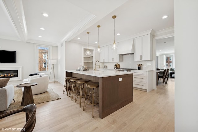 4256 N Keeler Ave, Chicago, IL 60641 - kitchen with custom exhaust hood, light wood-style floors, white cabinetry, a breakfast bar, and open floor plan