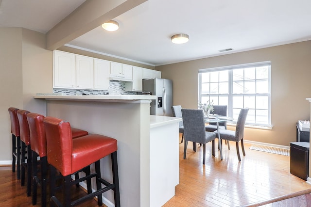 2276 Vanderbilt Dr Unit 2276, Geneva, IL 60134 - kitchen with stainless steel fridge with ice dispenser, a kitchen breakfast bar, white cabinets, light wood-style flooring, and crown molding