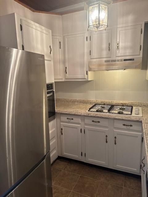 509 N Quincy St, Clinton, IL 61727 - kitchen featuring appliances with stainless steel finishes, under cabinet range hood, white cabinets, dark tile patterned floors, and a chandelier