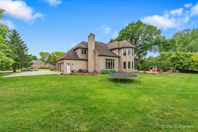 7530 Inverway Dr, Lakewood, IL 60014 - rear view of property with a trampoline, a chimney, driveway, and a lawn