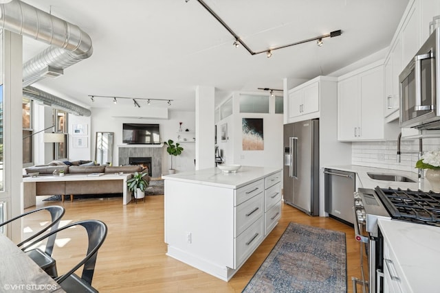 1001 W Madison St Unit 211, Chicago, IL 60607 - kitchen featuring stainless steel appliances, rail lighting, a tile fireplace, and white cabinets