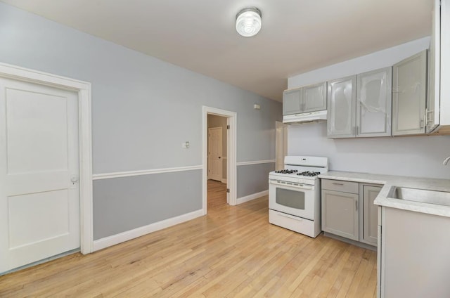 6834 S Rockwell St, Chicago, IL 60629 - kitchen with white gas range, a sink, gray cabinetry, under cabinet range hood, and light wood-style floors
