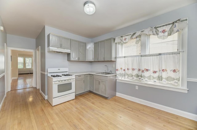 6834 S Rockwell St, Chicago, IL 60629 - kitchen with white range with gas stovetop, gray cabinetry, under cabinet range hood, a sink, and radiator heating unit