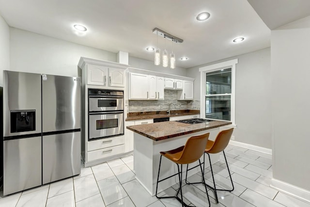 614 E 92nd Pl, Chicago, IL 60619 - kitchen with appliances with stainless steel finishes, white cabinets, decorative backsplash, a breakfast bar, and a kitchen island