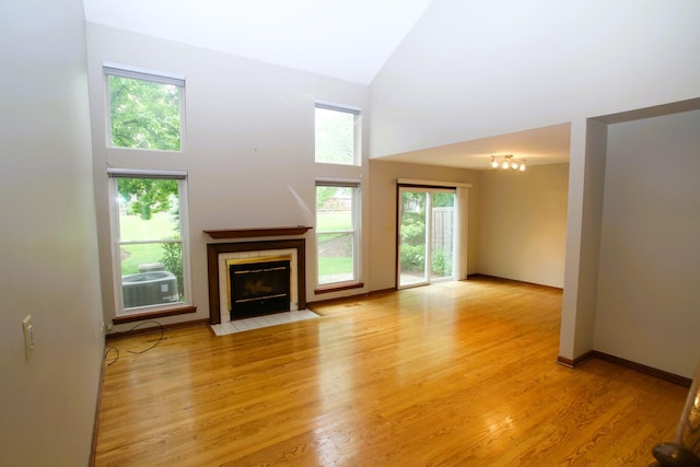 176 Millers Xing, Itasca, IL 60143 - unfurnished living room with a tiled fireplace, light wood-style flooring, a towering ceiling, and baseboards