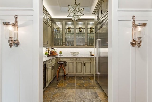 bar featuring stainless steel built in refrigerator, dark stone finish floors, backsplash, a chandelier, and a tray ceiling