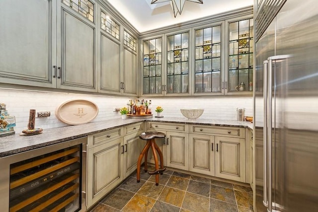 indoor dry bar featuring wine cooler, stainless steel built in refrigerator, stone tile floors, and tasteful backsplash