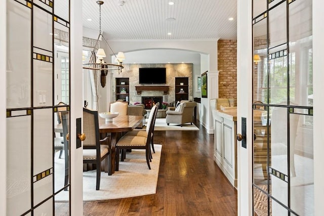 dining room featuring dark wood-style flooring, a lit fireplace, recessed lighting, arched walkways, and a chandelier