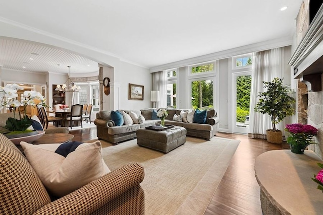 living area featuring plenty of natural light, wood finished floors, a chandelier, crown molding, and arched walkways