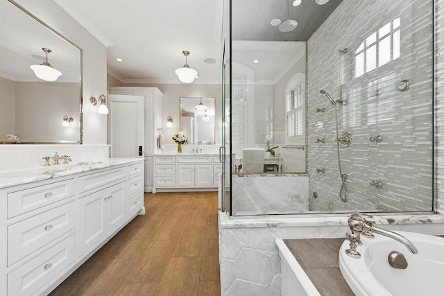 bathroom featuring ornamental molding, a shower stall, two vanities, a bath, and wood finished floors