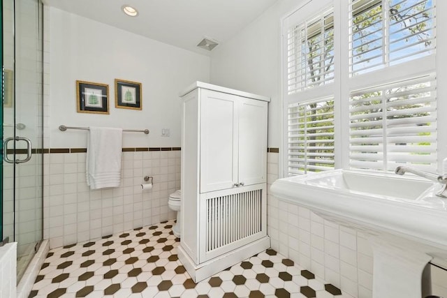 bathroom with a stall shower, tile walls, tile patterned floors, and wainscoting