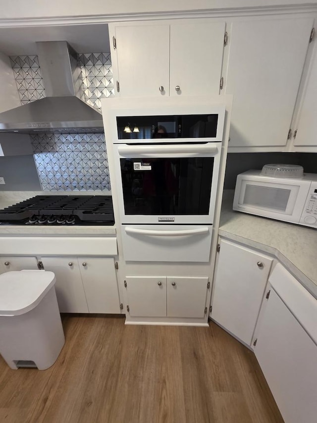6124 W Berteau Ave, Chicago, IL 60634 - kitchen featuring wall chimney range hood, white appliances, light wood-style flooring, a warming drawer, and white cabinets