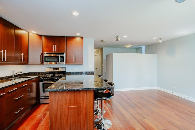 3441 W Grace St Unit G, Chicago, IL 60618 - kitchen featuring stainless steel appliances, a breakfast bar, light wood-type flooring, dark stone counters, and a sink