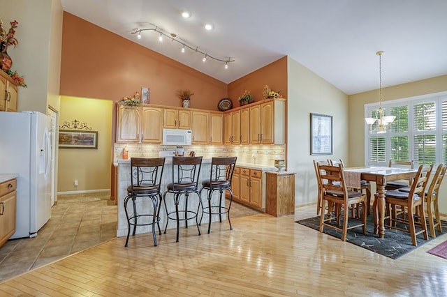 608 Bridgeman Ln, Romeoville, IL 60446 - kitchen with white appliances, a breakfast bar area, tasteful backsplash, high vaulted ceiling, and a chandelier