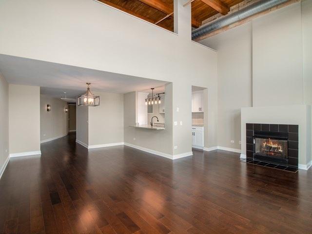 50 E 26th St Unit 406, Chicago, IL 60616 - unfurnished living room featuring a towering ceiling, a chandelier, dark wood-style flooring, a tiled fireplace, and baseboards