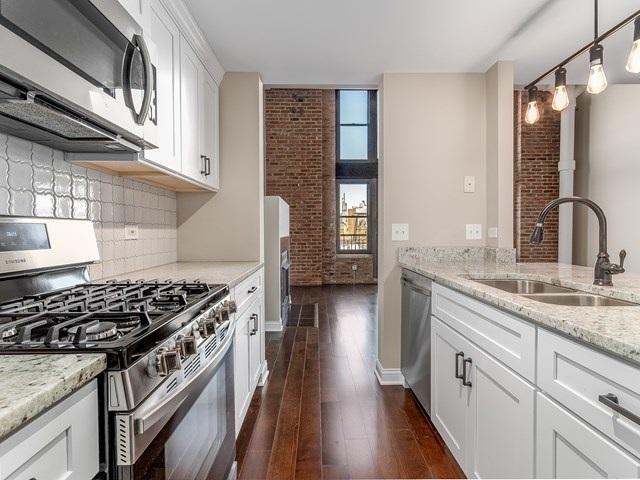50 E 26th St Unit 406, Chicago, IL 60616 - kitchen with stainless steel appliances, a sink, brick wall, tasteful backsplash, and dark wood-style flooring