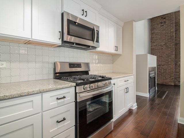 50 E 26th St Unit 406, Chicago, IL 60616 - kitchen with stainless steel appliances, dark wood-style floors, light stone counters, white cabinetry, and tasteful backsplash