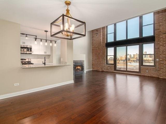 50 E 26th St Unit 406, Chicago, IL 60616 - unfurnished living room with baseboards, a chandelier, dark wood-style floors, rail lighting, and brick wall