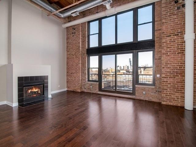 50 E 26th St Unit 406, Chicago, IL 60616 - unfurnished living room featuring a towering ceiling, wood finished floors, brick wall, a fireplace, and healthy amount of natural light