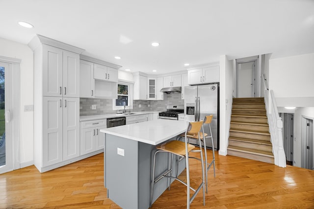 3795 Whispering Trails Dr, Hoffman Estates, IL 60192 - kitchen featuring stainless steel appliances, under cabinet range hood, a breakfast bar area, a center island, and light wood finished floors