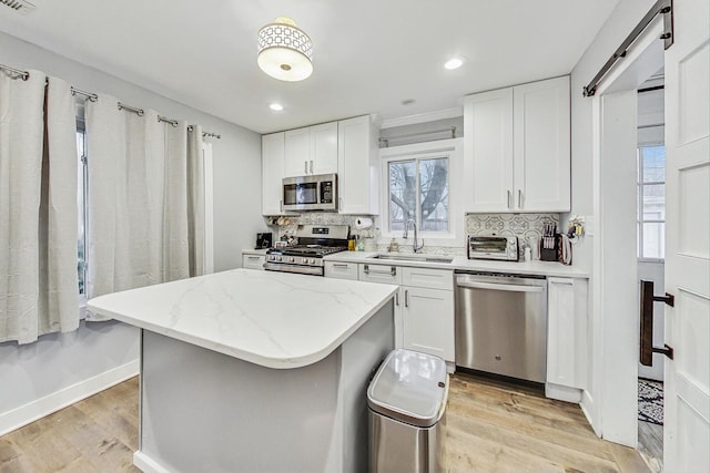 1049 Fowler Ave, Evanston, IL 60202 - kitchen featuring stainless steel appliances, a sink, a kitchen island, light wood finished floors, and white cabinets