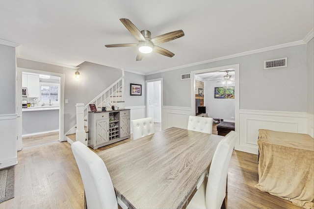 1049 Fowler Ave, Evanston, IL 60202 - dining area with a ceiling fan, stairs, crown molding, a wainscoted wall, and light wood-style flooring