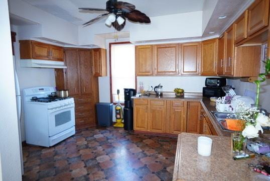 1711 S 4th St, Rockford, IL 61104 - kitchen featuring white gas range, under cabinet range hood, ceiling fan, and brown cabinetry