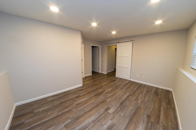2433 River Oaks Ln Unit 6, Rockford, IL 61102 - unfurnished bedroom featuring a barn door, dark wood-style flooring, baseboards, and recessed lighting