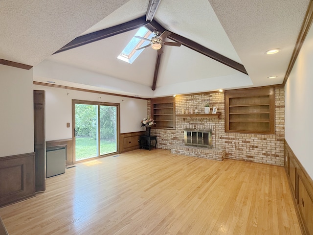 1463 Lantern Cir, Naperville, IL 60540 - unfurnished living room featuring a wainscoted wall, a textured ceiling, light wood-style floors, a skylight, and a brick fireplace