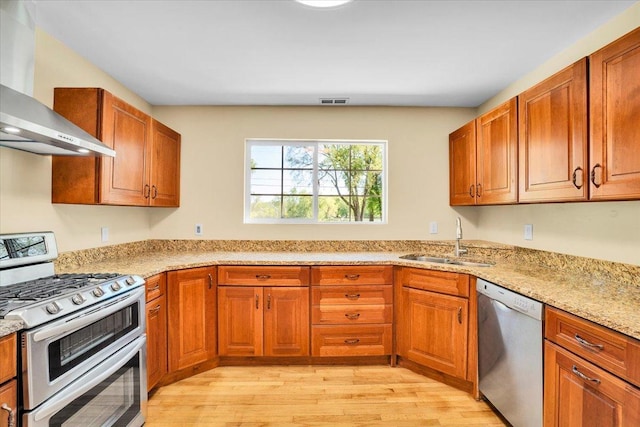 2425 W Riverside Dr, Mchenry, IL 60050 - kitchen featuring stainless steel appliances, wall chimney range hood, a sink, light wood-style flooring, and brown cabinetry
