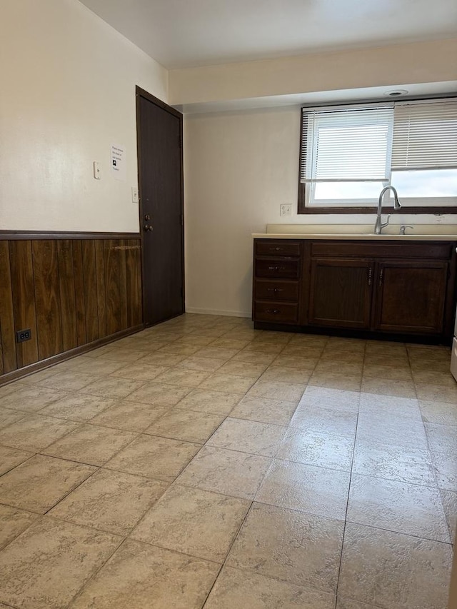 4100 Cove Ln Unit F, Glenview, IL 60025 - kitchen with dark brown cabinets, wainscoting, a sink, light countertops, and wooden walls