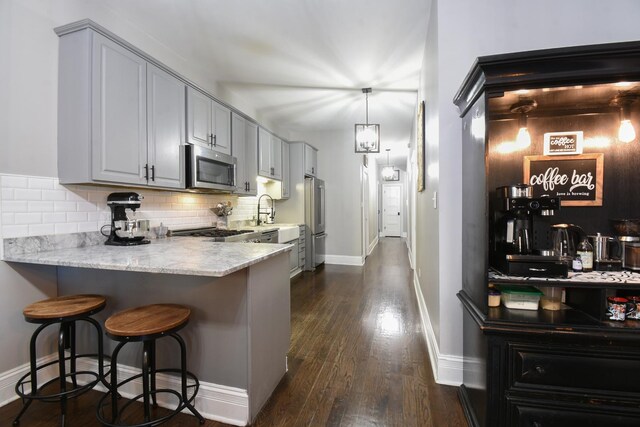 4419 N Racine Ave Unit 1N, Chicago, IL 60640 - kitchen featuring appliances with stainless steel finishes, decorative backsplash, dark wood-style floors, a breakfast bar, and a peninsula