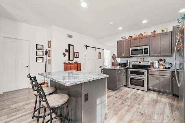6010 Peart Rd, Morris, IL 60450 - kitchen featuring stainless steel appliances, light wood-style flooring, a breakfast bar, light stone counters, and a barn door