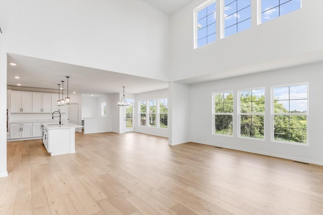 28 Open Pkwy, Hawthorn Woods, IL 60047 - unfurnished living room featuring a chandelier, light wood-style flooring, a sink, a towering ceiling, and recessed lighting