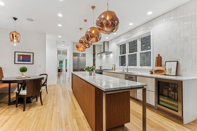 kitchen with beverage cooler, modern cabinets, wall chimney range hood, stainless steel appliances, and a kitchen island