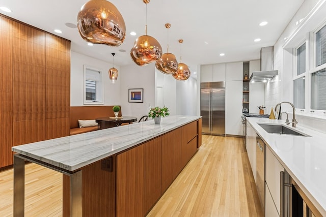 kitchen featuring appliances with stainless steel finishes, modern cabinets, wall chimney exhaust hood, light wood-type flooring, and recessed lighting