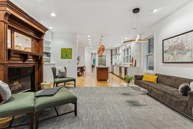 living room with a warm lit fireplace, recessed lighting, and light wood-type flooring