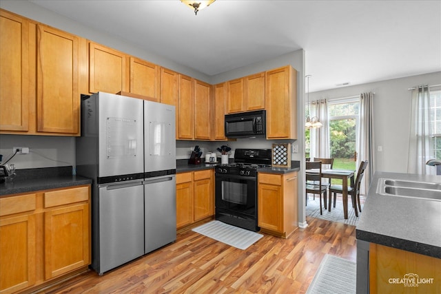 616 Springbrook Trl N, Oswego, IL 60543 - kitchen with black appliances, a sink, light wood-style flooring, dark countertops, and a chandelier