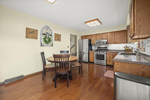 175 N Dogwood St, Cortland, IL 60112 - kitchen with stainless steel appliances, a sink, brown cabinetry, dark countertops, and dark wood finished floors