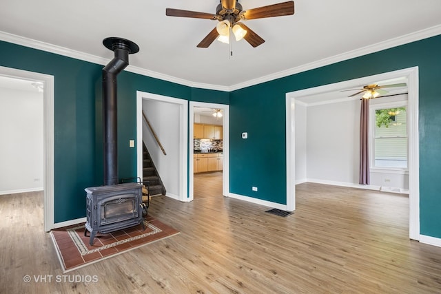 374 E Crystal Lake Ave, Crystal Lake, IL 60014 - unfurnished living room featuring a wood stove, wood finished floors, crown molding, ceiling fan, and baseboards