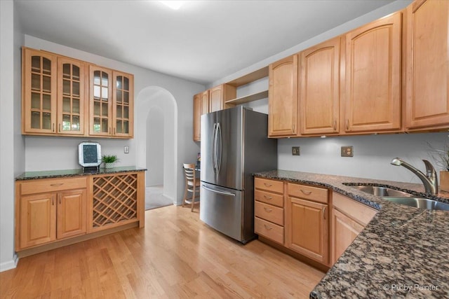 324 Torrington Dr, Bloomingdale, IL 60108 - kitchen featuring a sink, arched walkways, freestanding refrigerator, light wood-style floors, and dark stone countertops