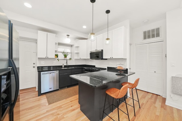3406 W Medill Ave Unit 1, Chicago, IL 60647 - kitchen with stainless steel appliances, open shelves, white cabinets, light wood-type flooring, and a kitchen breakfast bar