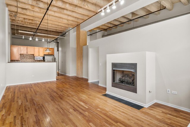 1645 W Ogden Ave Unit 304, Chicago, IL 60612 - unfurnished living room with rail lighting, a towering ceiling, light wood-type flooring, a fireplace with flush hearth, and baseboards