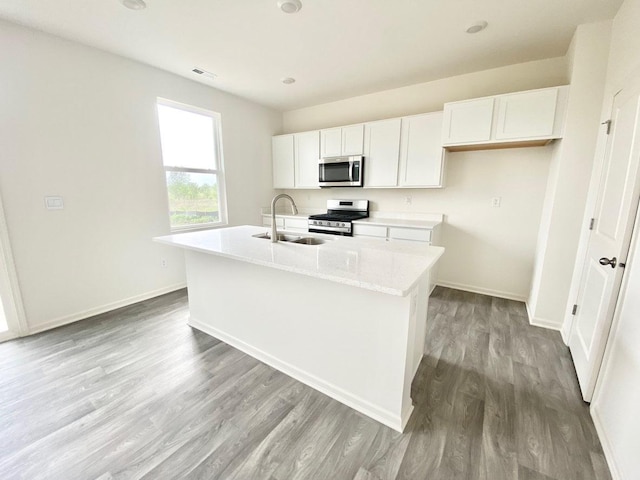 kitchen with stainless steel appliances, a sink, white cabinets, light wood-style flooring, and a center island with sink