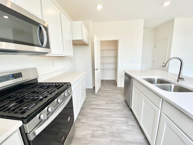 kitchen with appliances with stainless steel finishes, a sink, white cabinetry, light stone counters, and baseboards