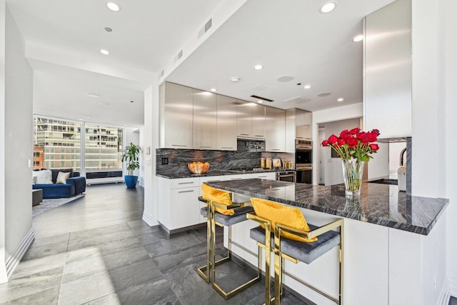 600 N Kingsbury Ave Unit 506, Chicago, IL 60610 - kitchen featuring a peninsula, recessed lighting, decorative backsplash, a kitchen bar, and dark stone countertops