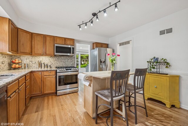 5513 Mulford St, Skokie, IL 60077 - kitchen featuring appliances with stainless steel finishes, light wood-type flooring, brown cabinets, and a kitchen breakfast bar